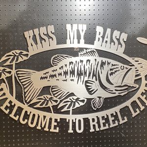 "Kiss My Bass" metal sign with a fish design, featuring "Welcome to Reel Life" text on dark perforated background.