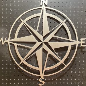 Metal compass rose wall art with cardinal directions, mounted on a perforated black pegboard.