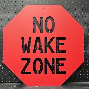 Red "No Wake Zone" metal sign with cutout text on a black pegboard background.