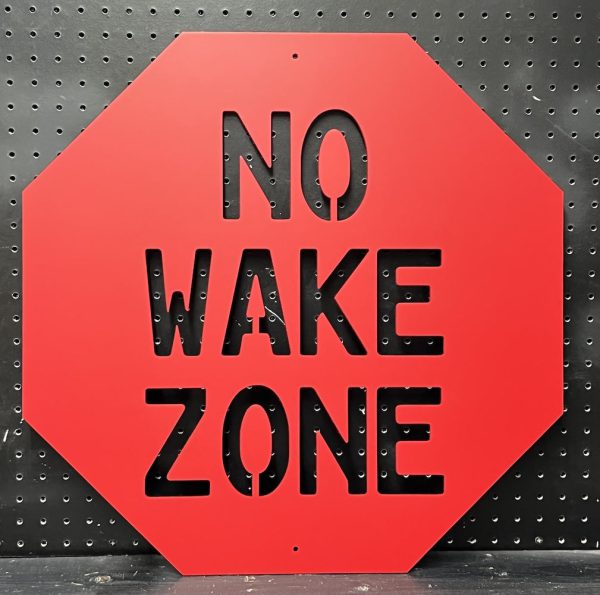 Red "No Wake Zone" metal sign with cutout text on a black pegboard background.