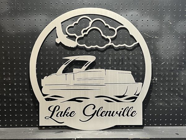 Lake Glenville metal sign with a pontoon design and cloud motif, mounted on a black pegboard background.