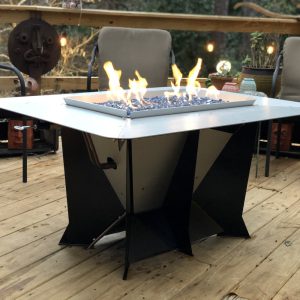 Modern gas fire pit with blue glass stones on a wooden deck, surrounded by chairs and string lights.