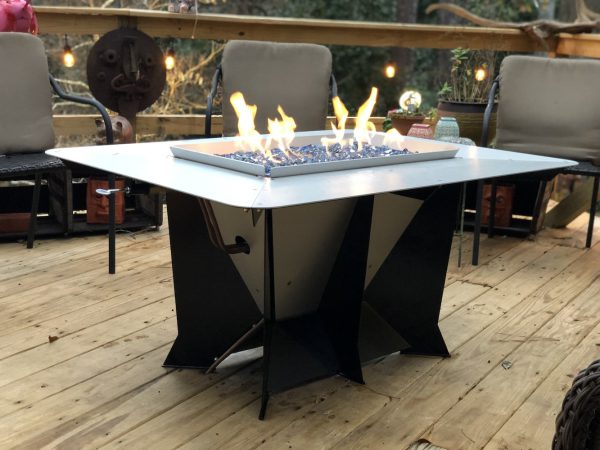 Modern gas fire pit with blue glass stones on a wooden deck, surrounded by chairs and string lights.