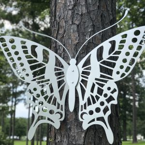 Intricate metal butterfly wall art on a tree with a lush forest backdrop.