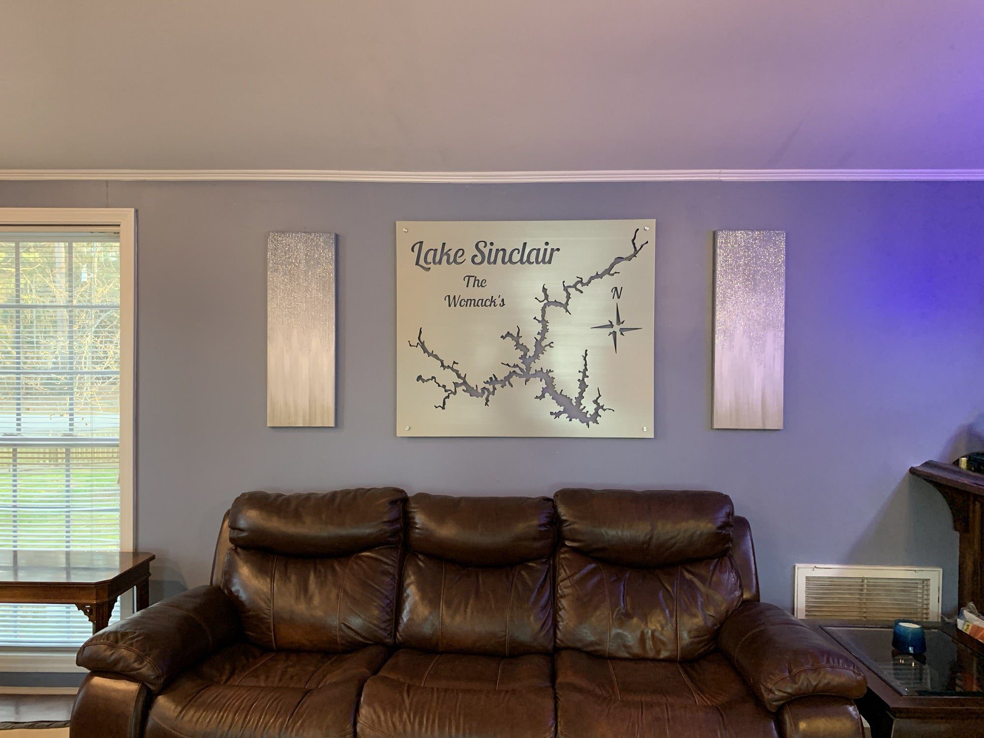 Lake Sinclair map with "The Womac's" text and compass rose, mounted above a leather sofa in a cozy living room.
