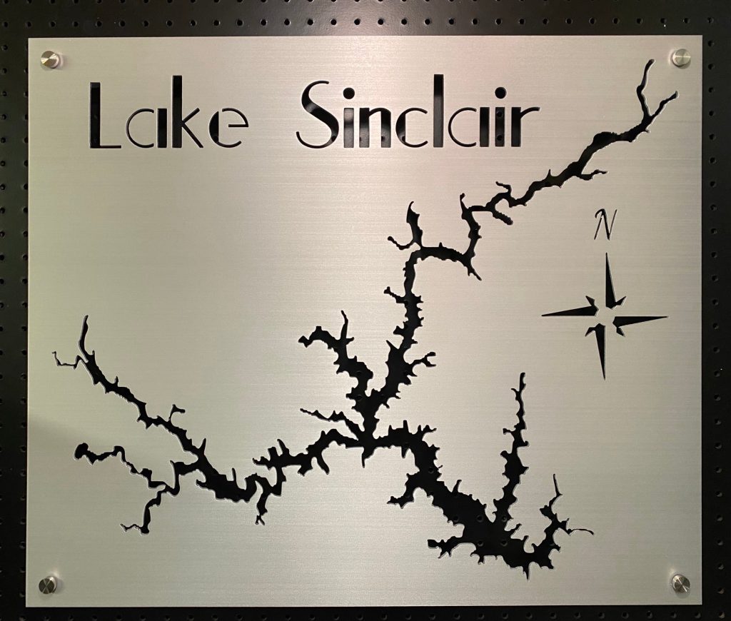 Lake Sinclair metal map sign with compass rose, mounted on a black pegboard.