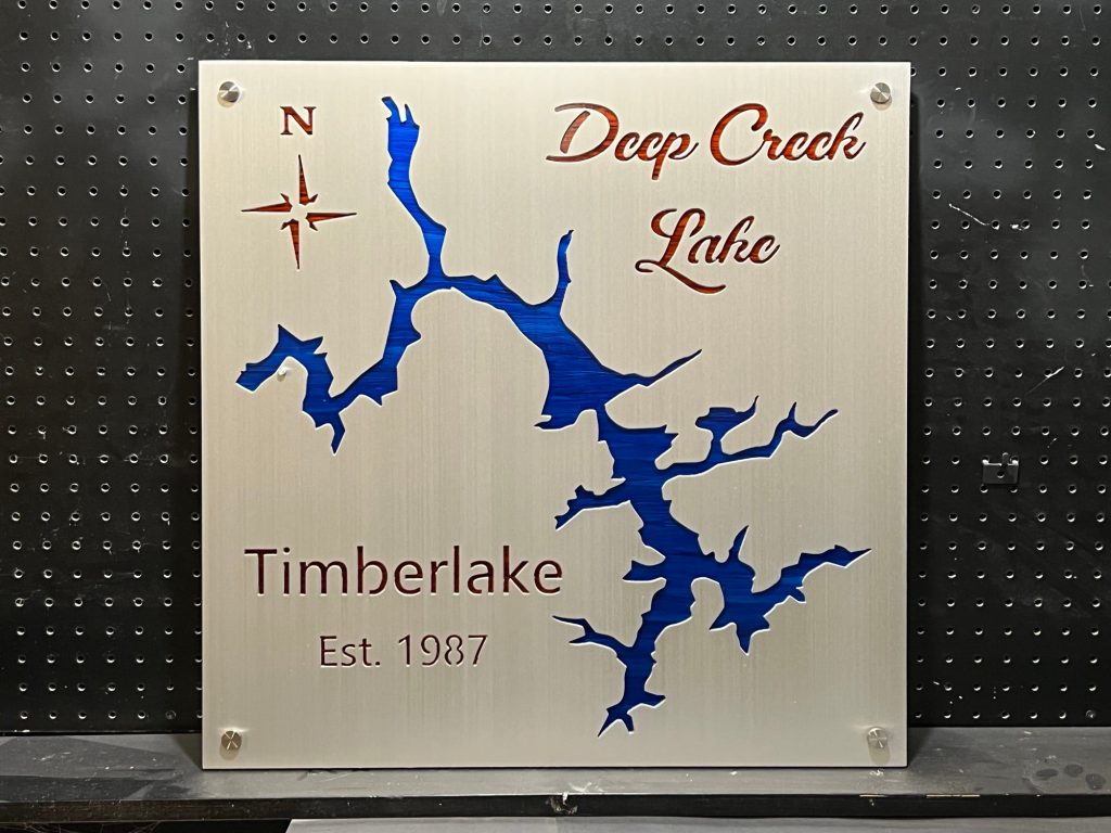 Deep Creek Lake metal map, "Timberlake Est. 1987," with compass rose, mounted on a perforated black background.