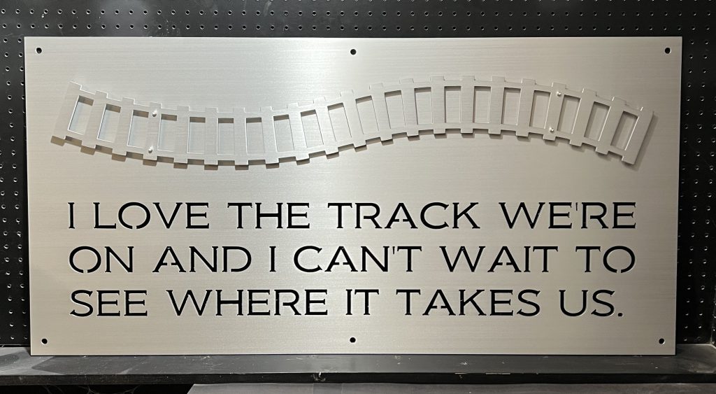 Metal sign with train track design and quote: "I love the track we're on and I can't wait to see where it takes us."