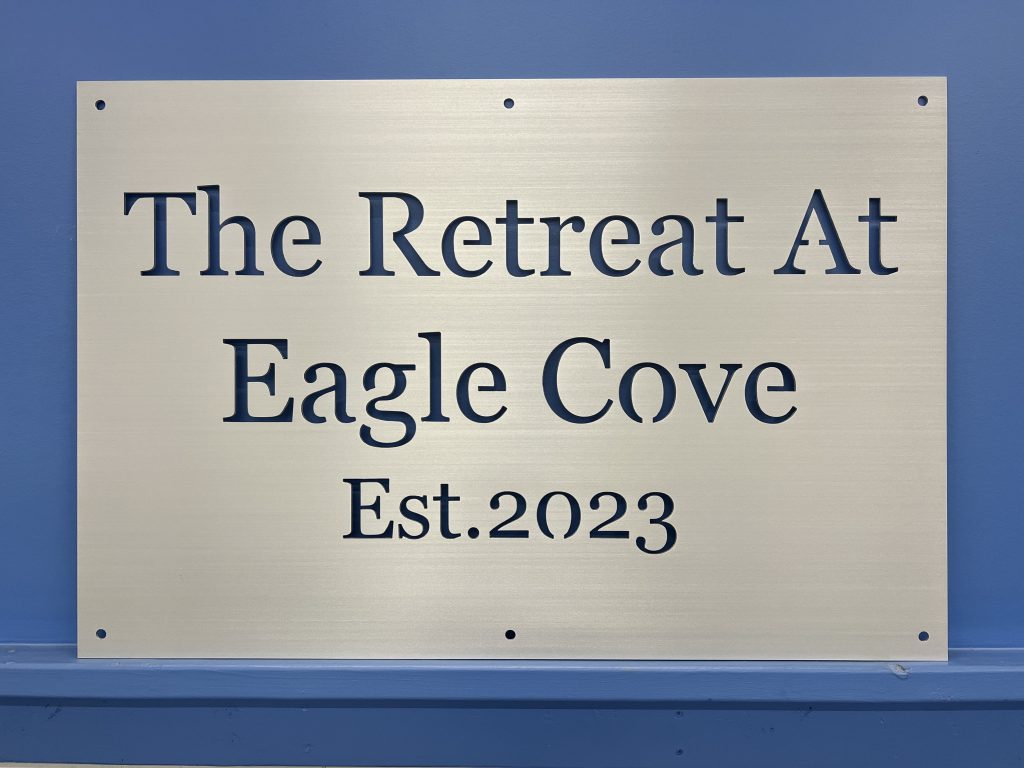 Metal sign with "The Retreat At Eagle Cove Est. 2023" text, mounted on a blue wall.