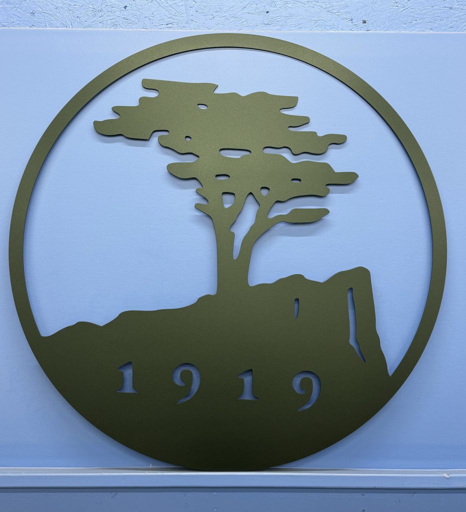 Metal sign with tree silhouette and "1919" cutout on a blue wall.