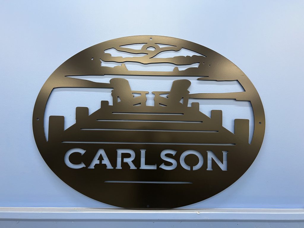 Custom metal sign with "Carlson" and a lake dock scene, mounted on a light blue wall.