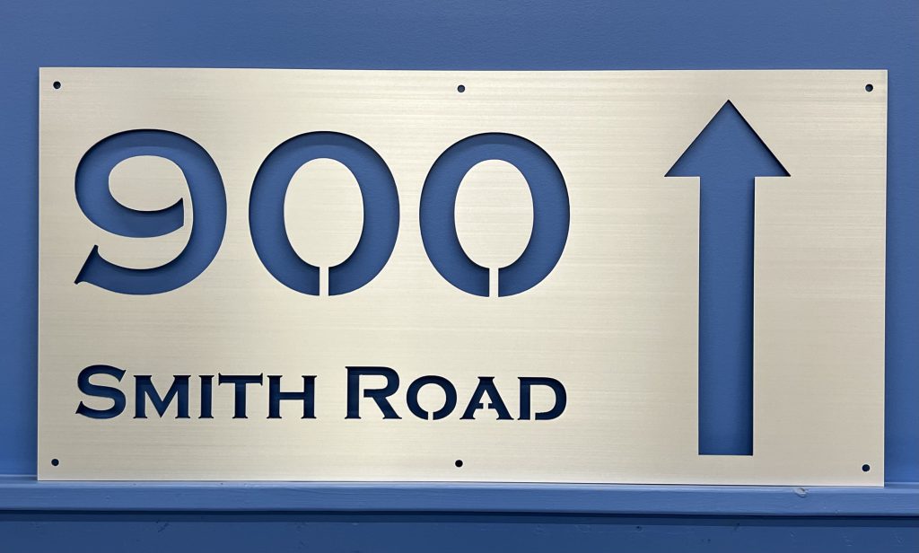 Custom metal sign with "900 Smith Road" and an upward arrow on a blue wall.