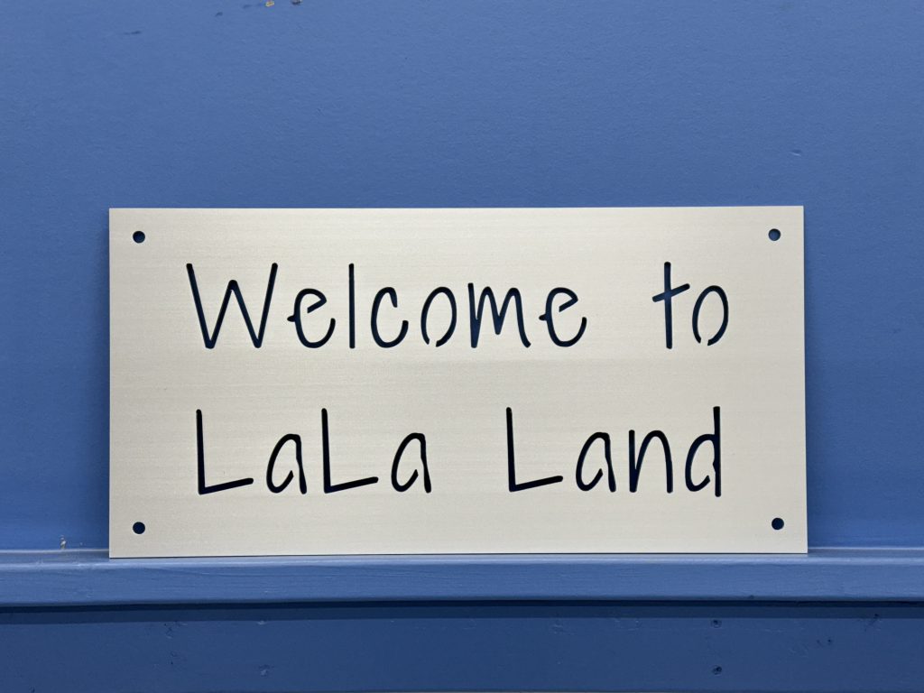 Metal sign with "Welcome to LaLa Land" text, mounted on a blue wall.