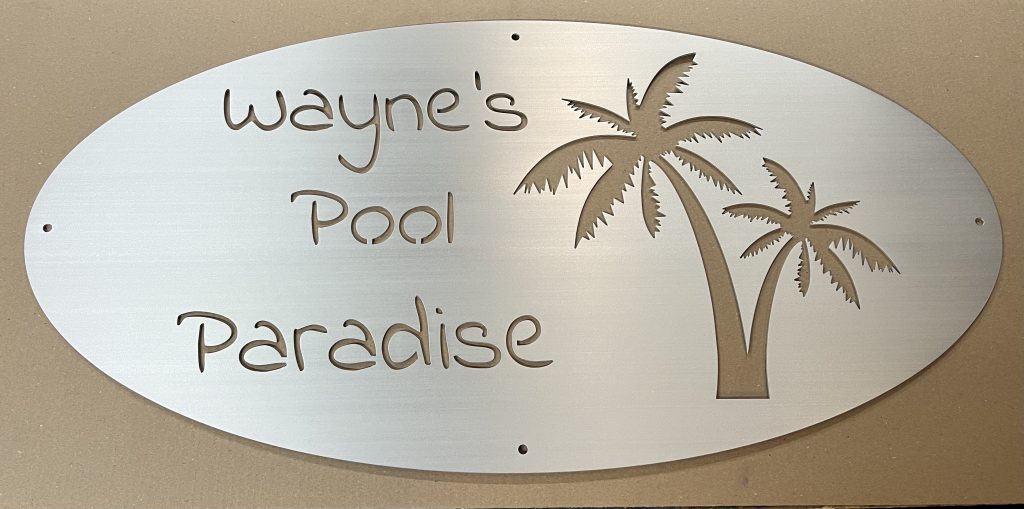 "Wayne's Pool Paradise" metal sign with palm tree cutout on brushed silver background.