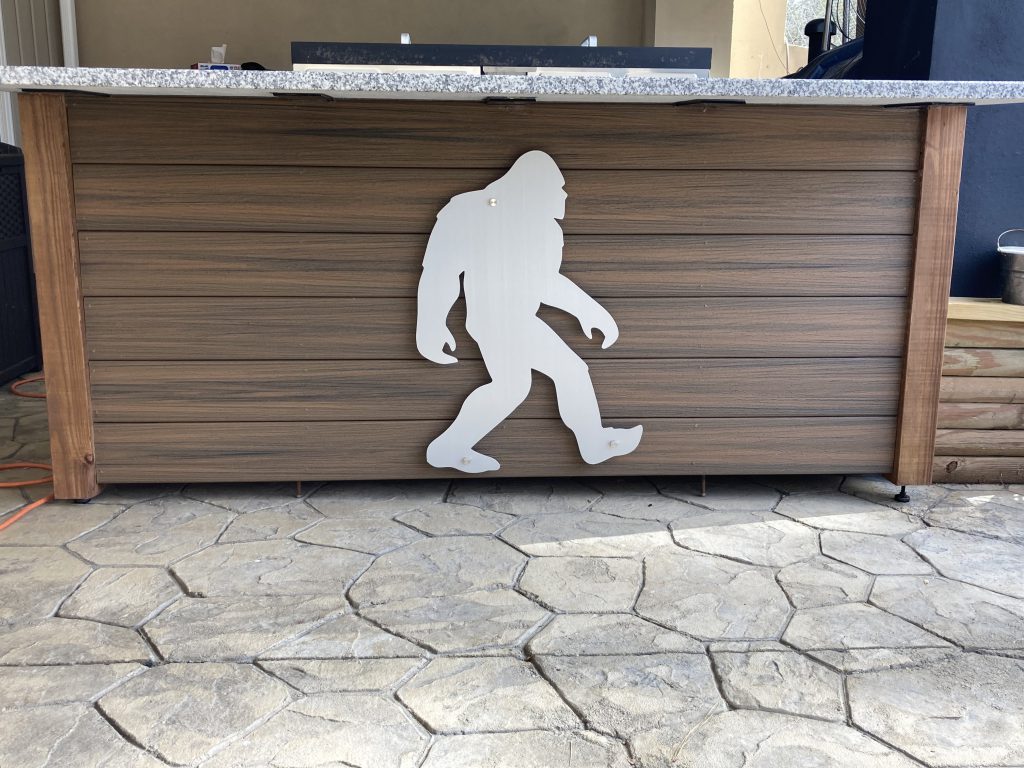 Custom Bigfoot metal sign on a wooden bar with a stone patio.