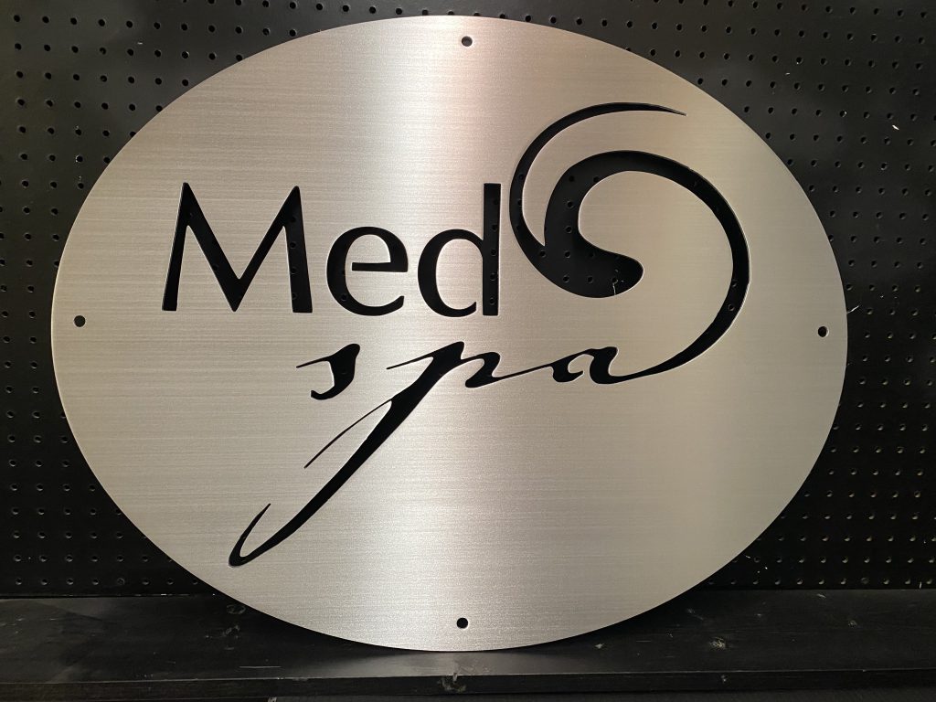 "Med Spa" metal sign with swirl design, mounted on a black pegboard.