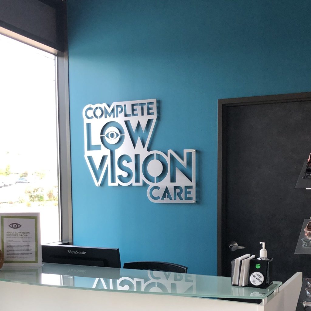 Complete Low Vision Care sign on a turquoise wall above a sleek reception desk.