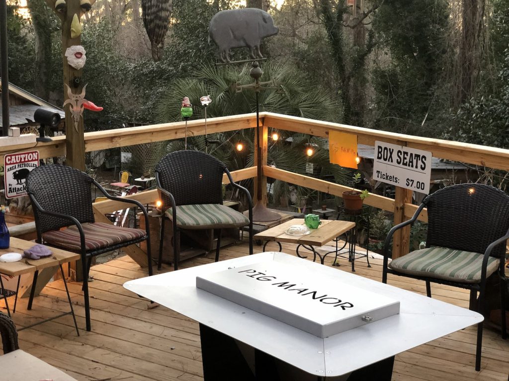 Cozy deck with "Pig Manor" firepit, chairs, and quirky decor, including a "Box Seats" sign for $7.00.