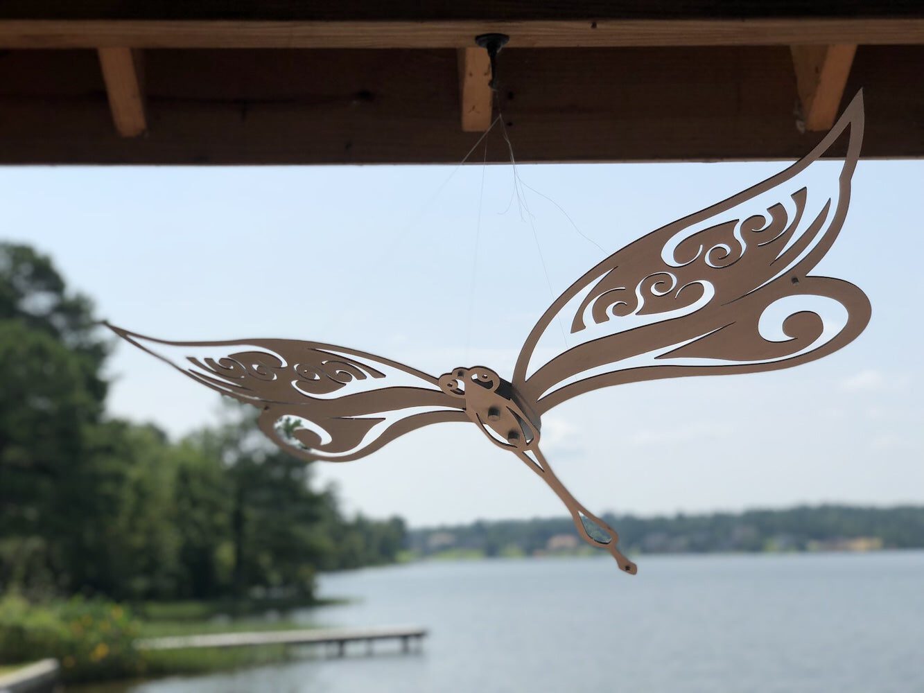 Intricate metal dragonfly hanging under a dock, with a serene lake view in the background.