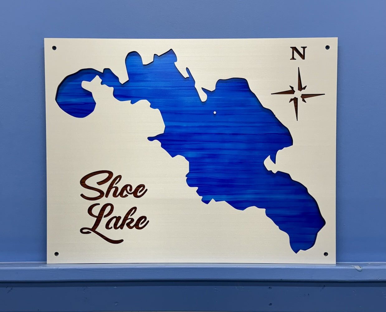 Shoe Lake metal map with blue cutout design and compass rose, mounted on a blue wall.