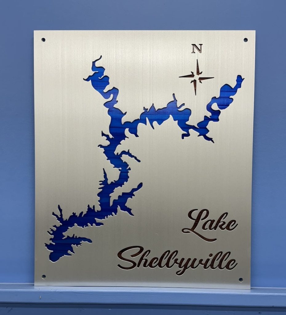 Lake Shelbyville metal map with blue cutout and compass rose, mounted on a blue wall.