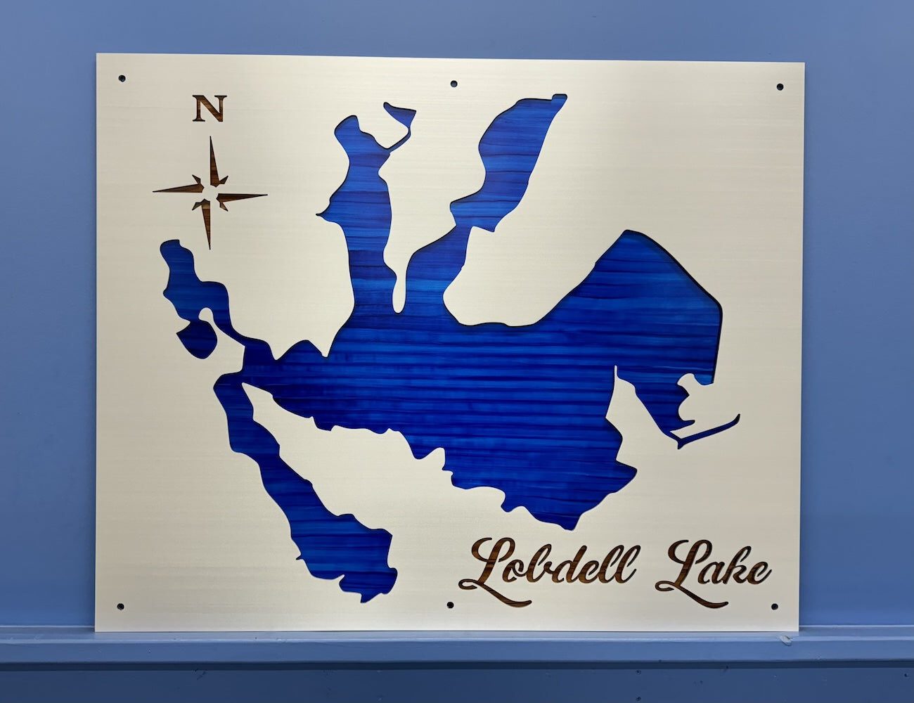 Lobdell Lake metal map with blue cutout and compass rose, mounted on a blue wall.