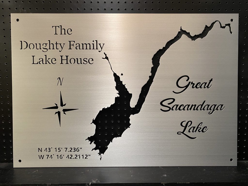 Custom metal map of Great Sacandaga Lake with coordinates, "The Doughty Family Lake House," on a perforated black background.