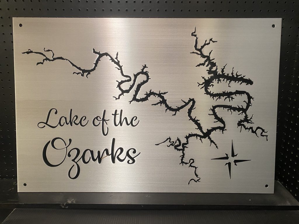 Lake of the Ozarks metal map sign with compass rose on brushed silver, mounted on a dark pegboard.