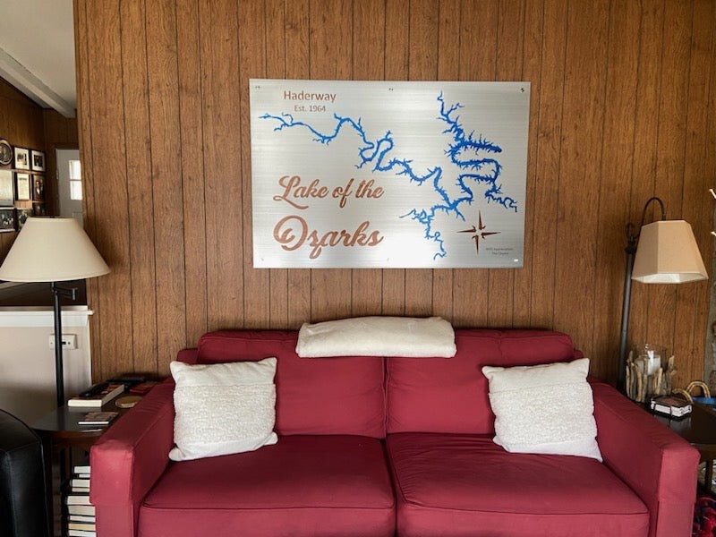 Lake of the Ozarks metal map with "Haderway Est. 1964" text, mounted above a red sofa in a wood-paneled room.