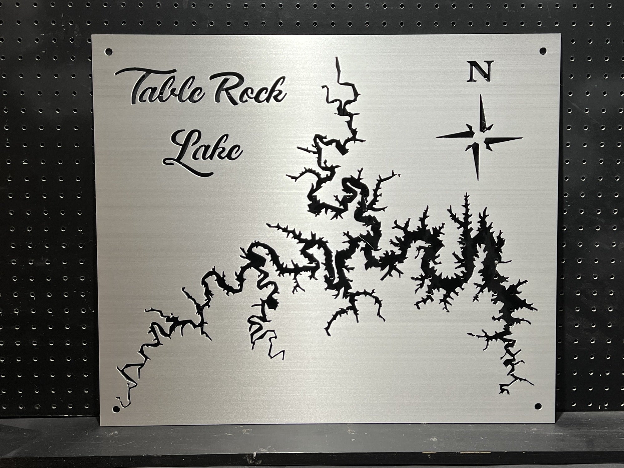 Table Rock Lake metal map with compass rose, featuring an intricate cutout design on brushed silver, mounted on a black pegboard.