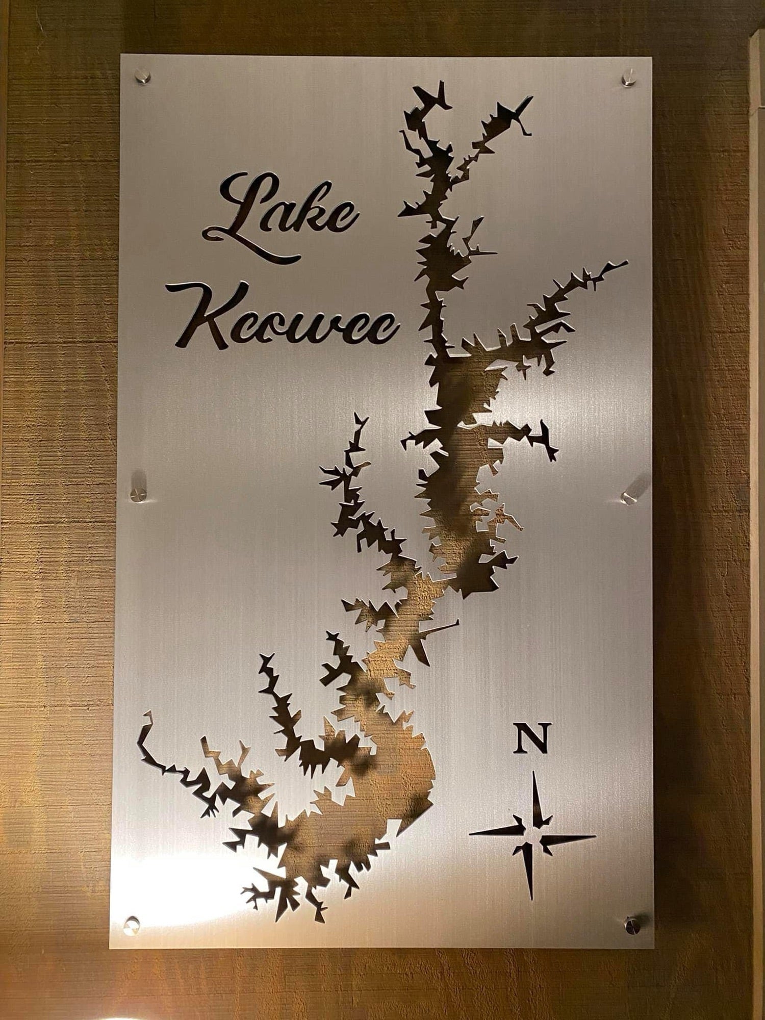 Brushed metal sign with Lake Keowee map cutout and compass rose, mounted on a wooden wall.