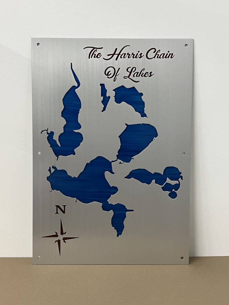 The Harris Chain of Lakes metal map with blue cutouts and compass rose on a brushed silver background.