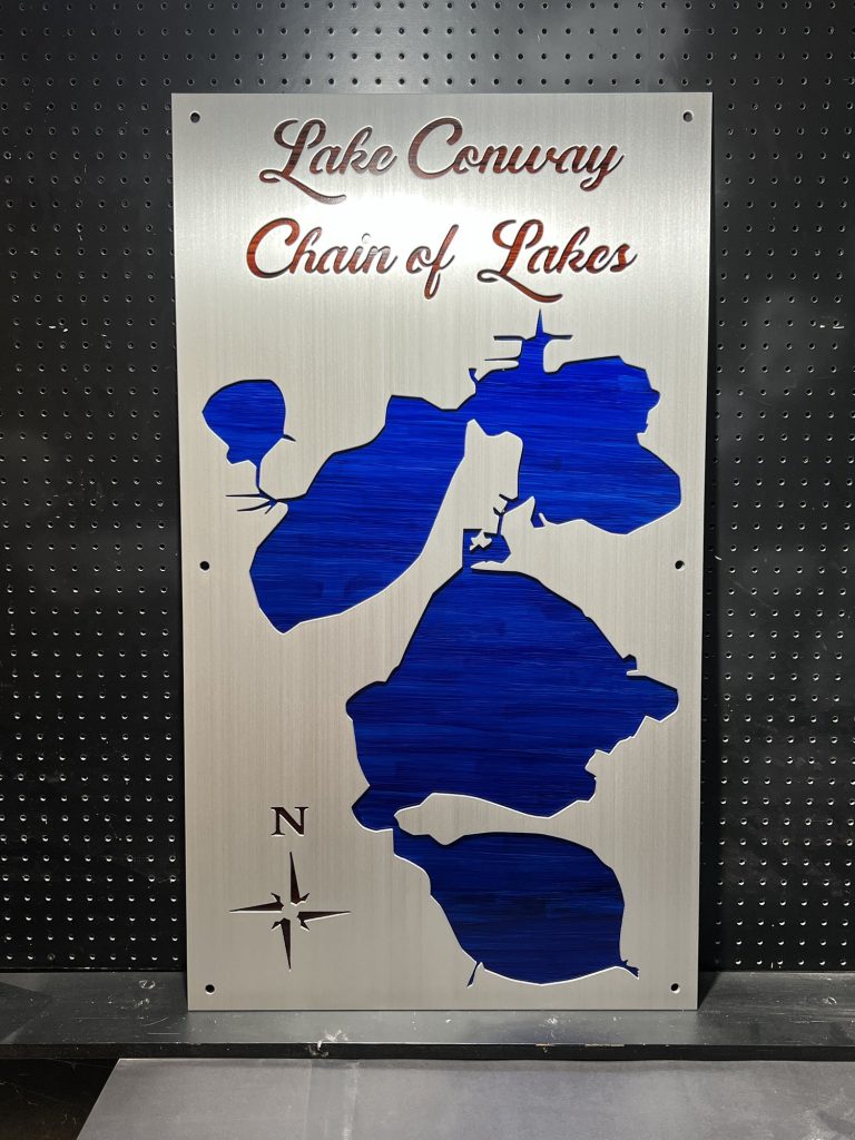 Lake Conway Chain of Lakes map on brushed metal with blue cutouts and compass rose on perforated background.