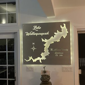 Metal map of Lake Wallenpaupack with compass and "The Hinman Family Lakehouse, Est. 2000," illuminated on a wall.