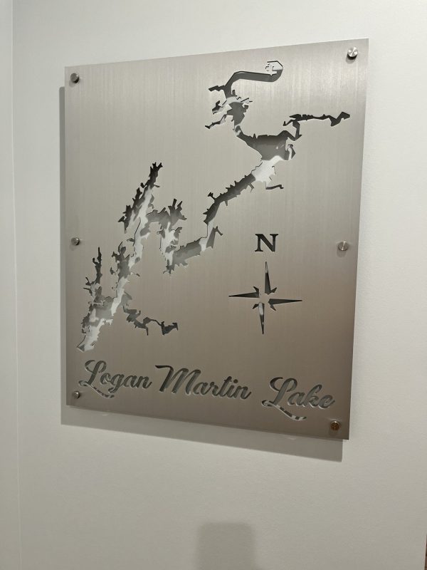 Metal map sign of Logan Martin Lake with compass design on a brushed background, mounted on a wall.