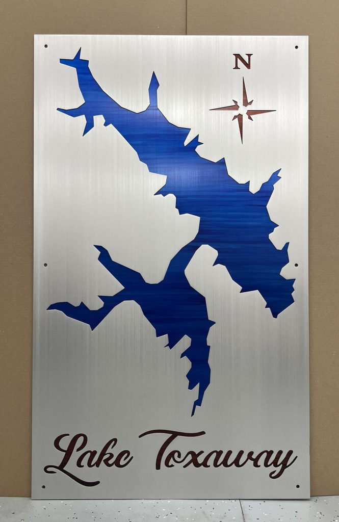 Lake Toxaway metal map with blue cutout and compass rose, on brushed silver background.