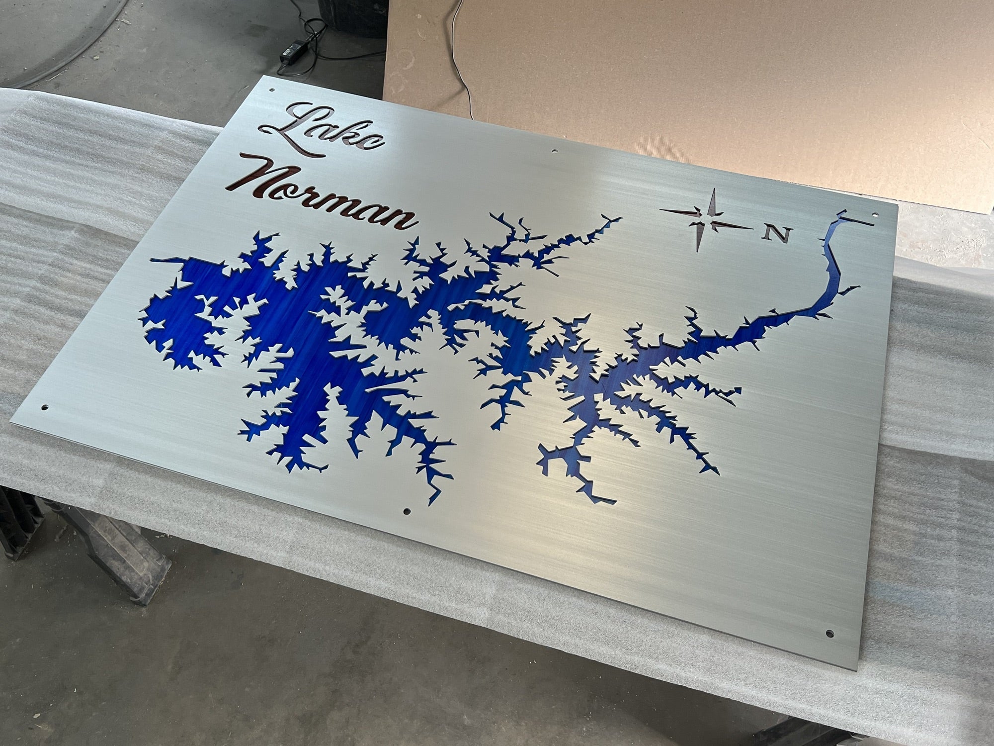 Lake Norman metal map with blue inlay and compass rose, displayed on a brushed metallic surface.