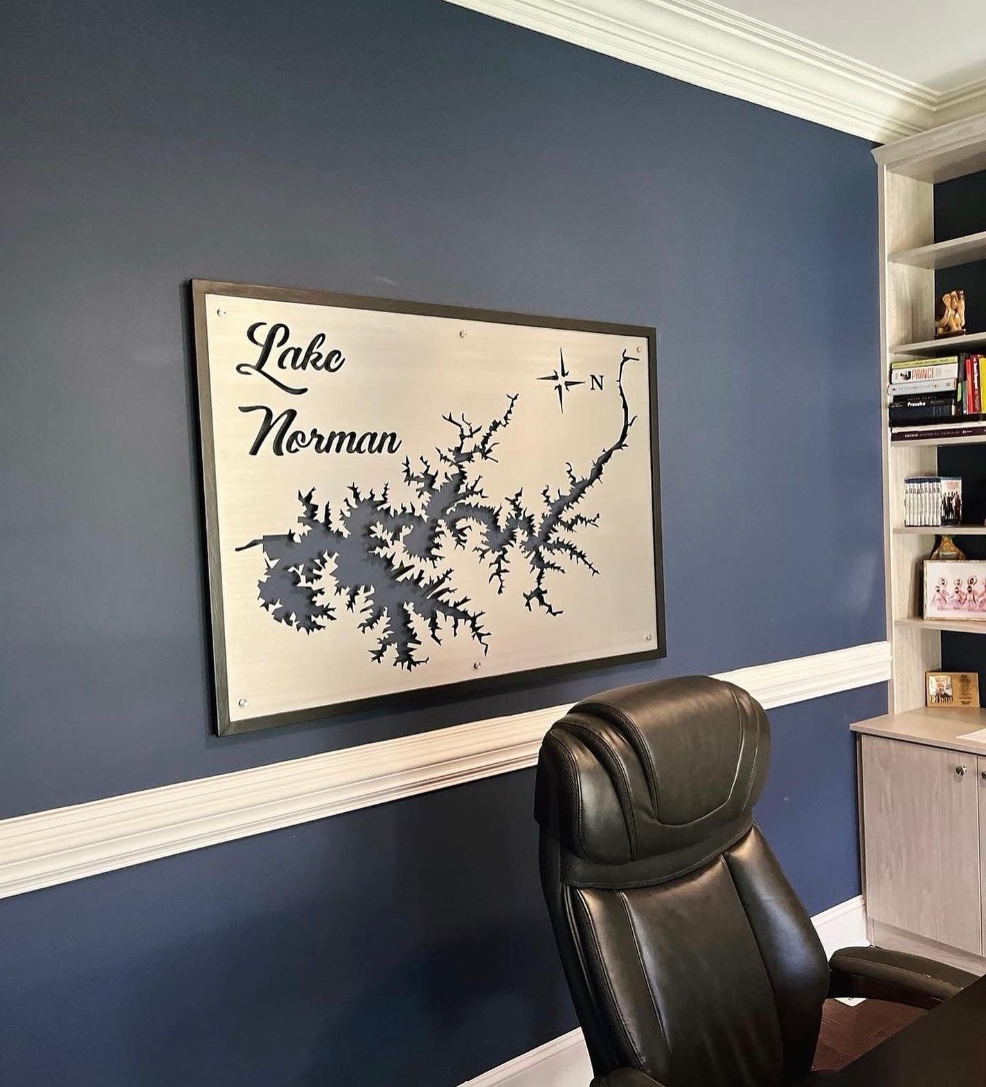 Lake Norman custom map with compass rose on a blue office wall, above a black leather chair.