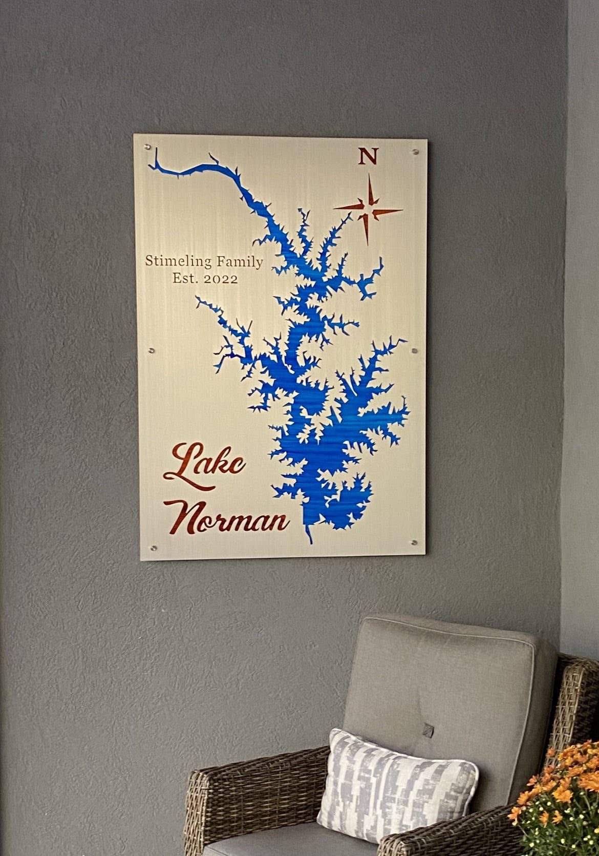 Lake Norman map with "Stimeling Family Est. 2022" text and compass rose, on a gray wall above a wicker chair.