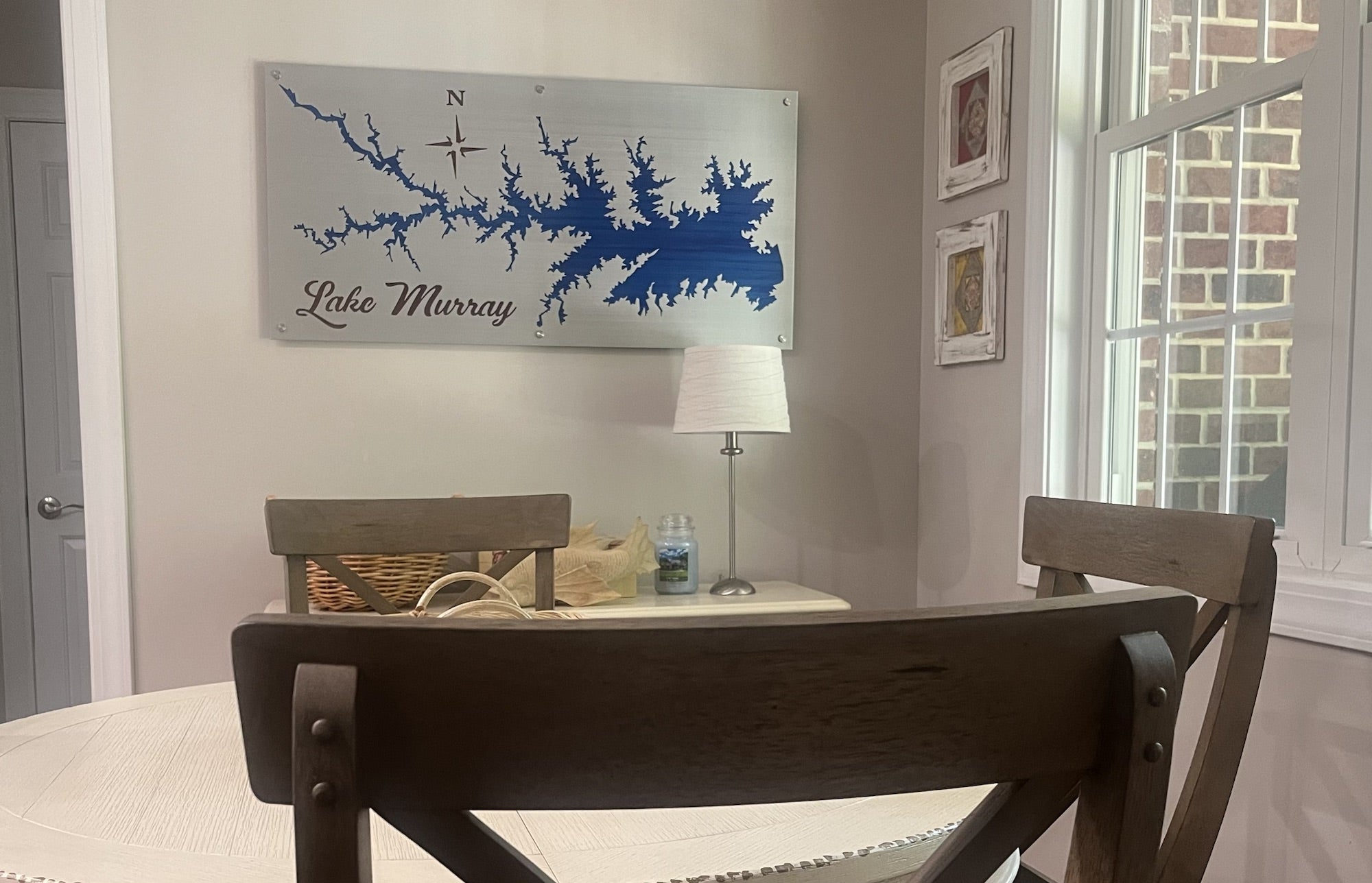 Lake Murray metal map with compass rose, mounted in a dining area with wooden chairs and a lamp.