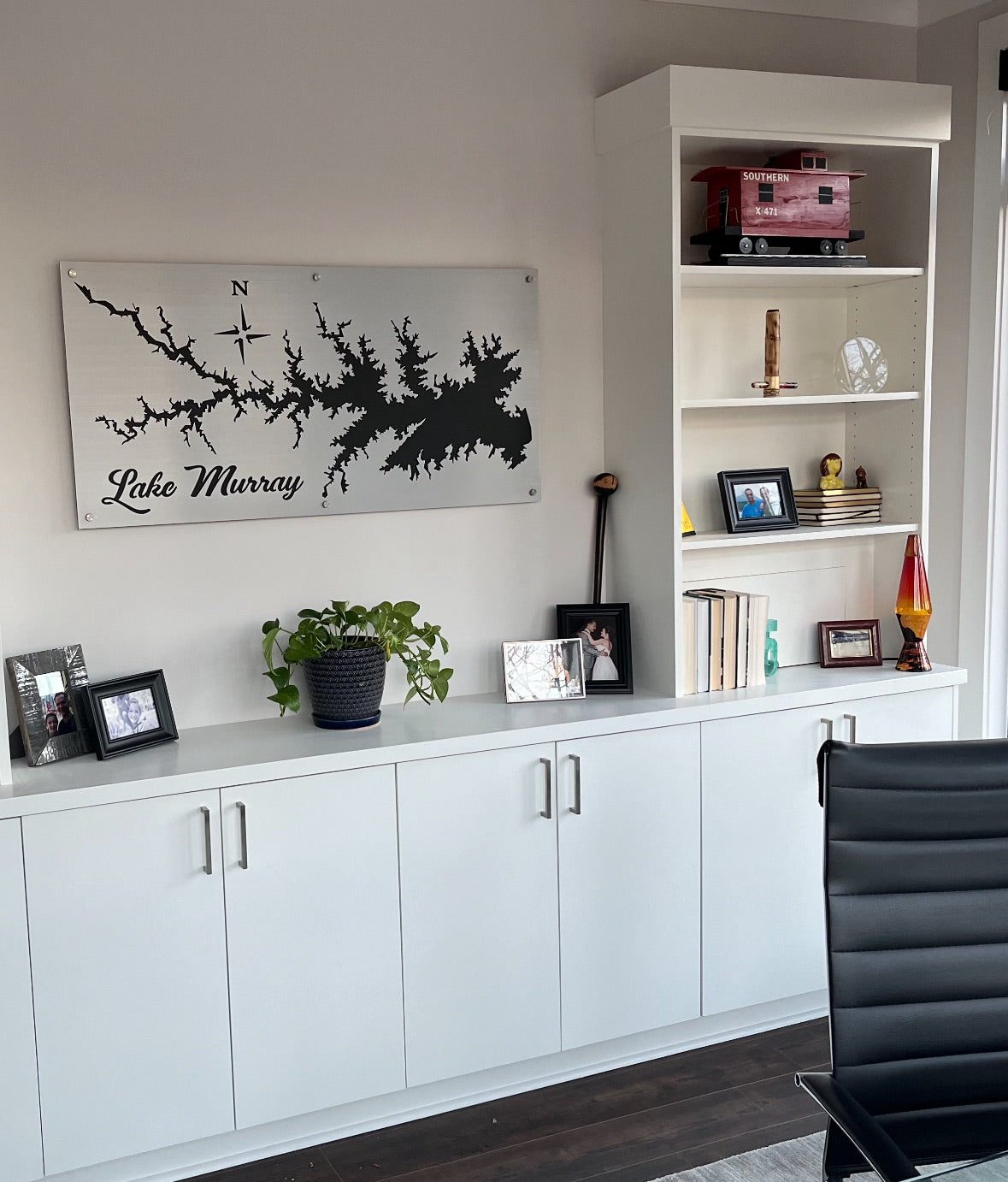 Lake Murray metal map with compass rose, mounted above white cabinets, next to a shelf with photos and decor.