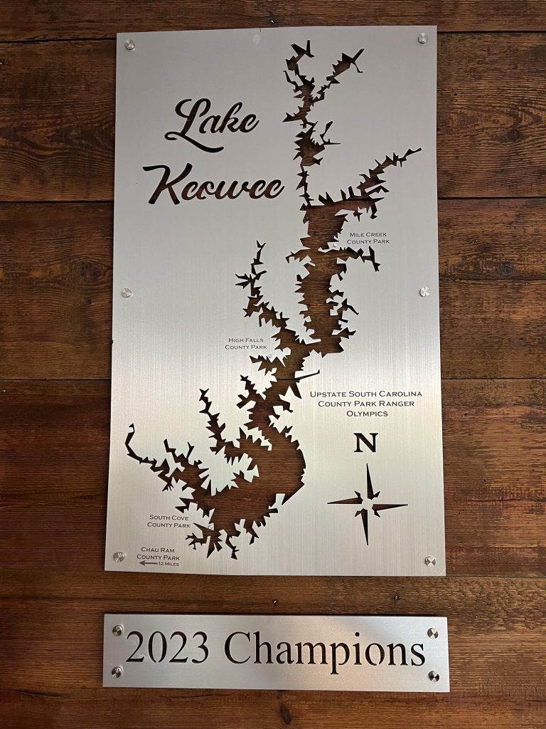 Lake Keowee custom metal sign with cutout design, compass rose, and "2023 Champions" on a wooden background.