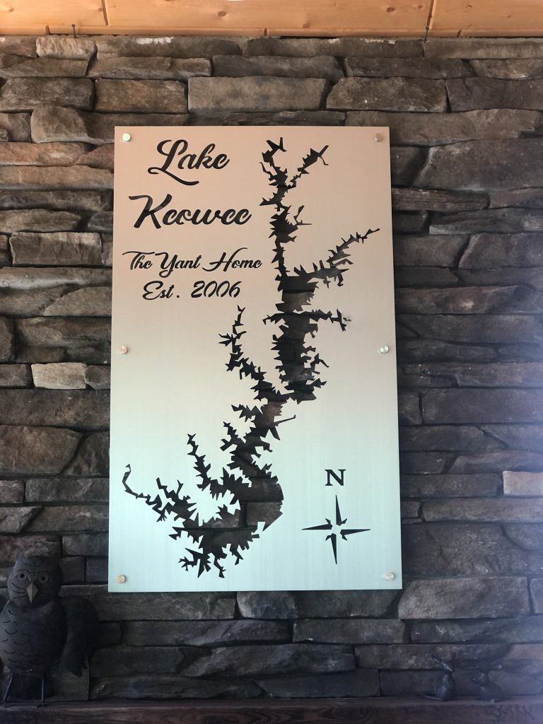 Lake Keowee metal map with intricate design and compass rose, mounted above a sofa on a grey wall.