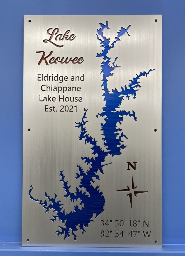 Lake Keowee metal sign for Eldridge and Chiappane Lake House, Est. 2021, with coordinates and compass rose on blue wall.