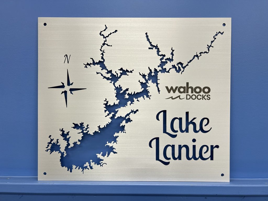 Brushed metal sign of Lake Lanier map with compass rose and Wahoo Docks logo on a blue wall.