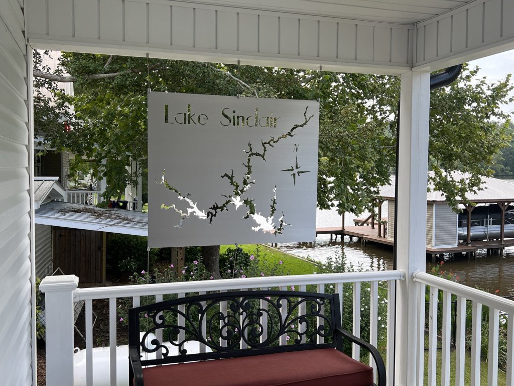 Lake Sinclair metal map with compass rose, hanging on a porch overlooking a dock and lake.