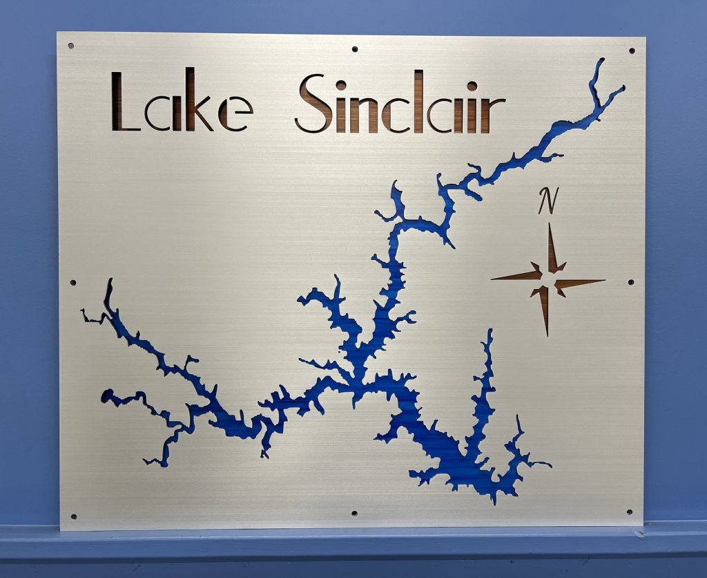 Lake Sinclair metal map with blue cutout and compass rose, mounted on a blue wall.