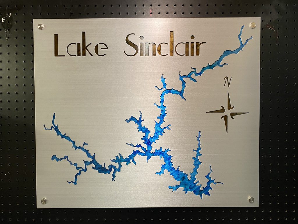 Lake Sinclair metal map with blue inlay and compass rose, mounted on a black pegboard.