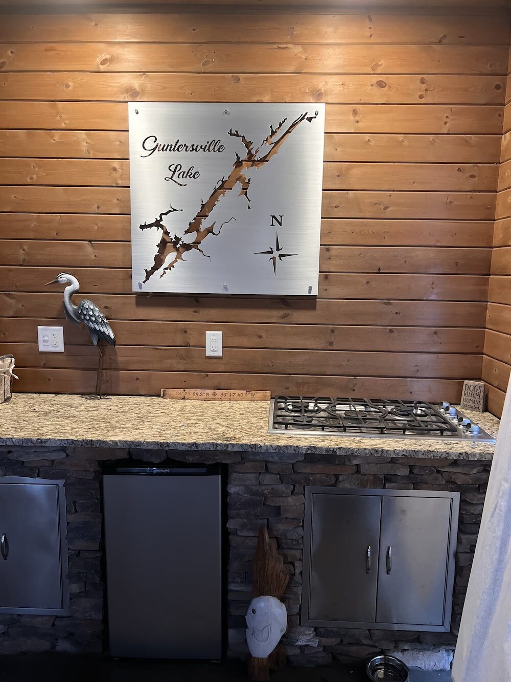 Guntersville Lake metal map with compass rose, mounted on a wooden kitchen wall above a stone countertop and stove.