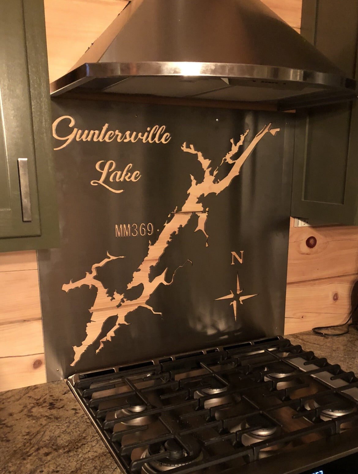 Guntersville Lake metal map backsplash with compass and "MM369" text above a kitchen stove.